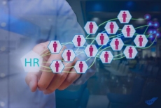 Grafika przedstawiająca dłoń osoby naciskającej ikonę z napisem ‘HR’, z której wychodzi sieć połączonych sześciokątnych ikon symbolizujących pracowników
