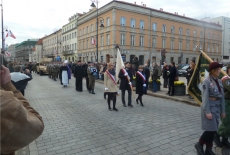 Środkiem ulicy idą żołnierze i ksiądz z trumną.