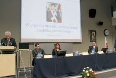 Dyrektor KSAP przemawia na mównicy, obok przy stole prezydialnym siedza paneliści