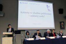 Pani stoi przy mównicy i przemawia, obok siedzą Paneliści przy stole 