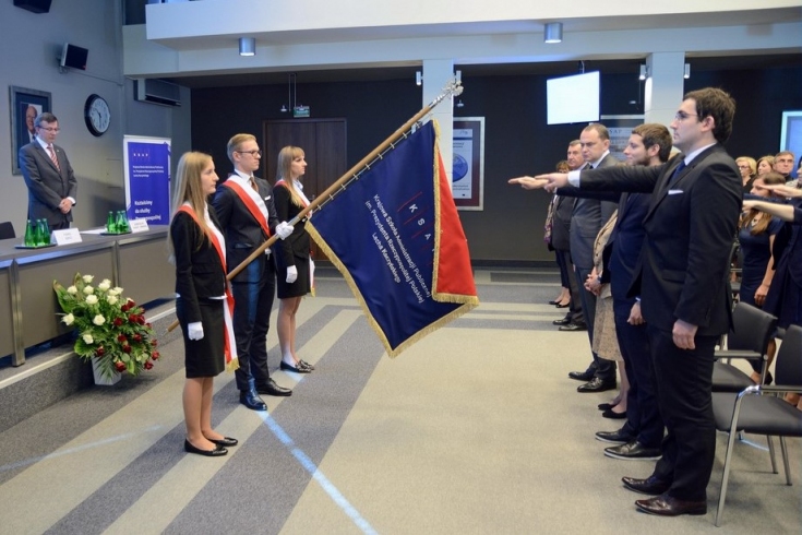 Na środku sali stoi trzyosobowa reprezentacja słuchaczy trzymająca sztandar KSAP, na wprost nich słuchacze KSAP podnosząc prawą rękę składają uroczystą przysięgę. 